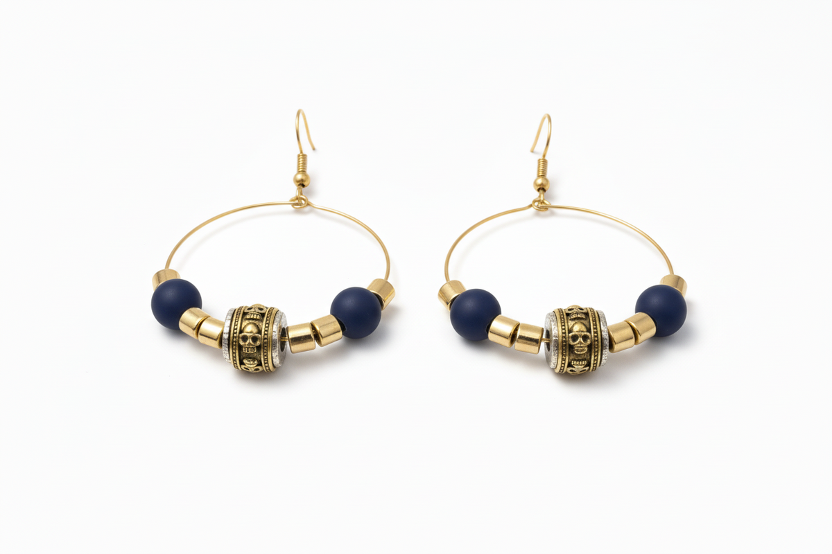 Gold wire hoop earrings with matte navy beads, ornate gold barrel bead, and gold spacer beads, shown on a textured neutral surface.