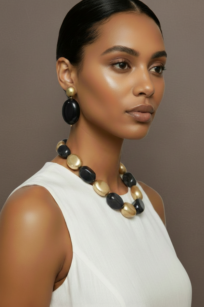 The Dior Statement Earrings, model wearing a chunky beaded necklace with alternating black and matte gold beads on a marble surface. ZoharasVogue
