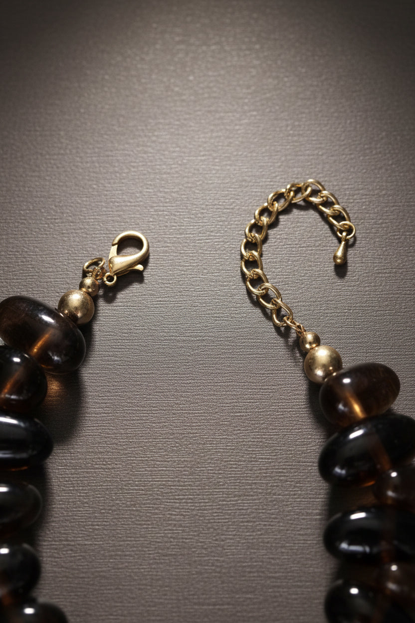 bold amber-toned statement necklace with layered beads and a textured oversized gold heart pendant styled with neutral fashion attire.