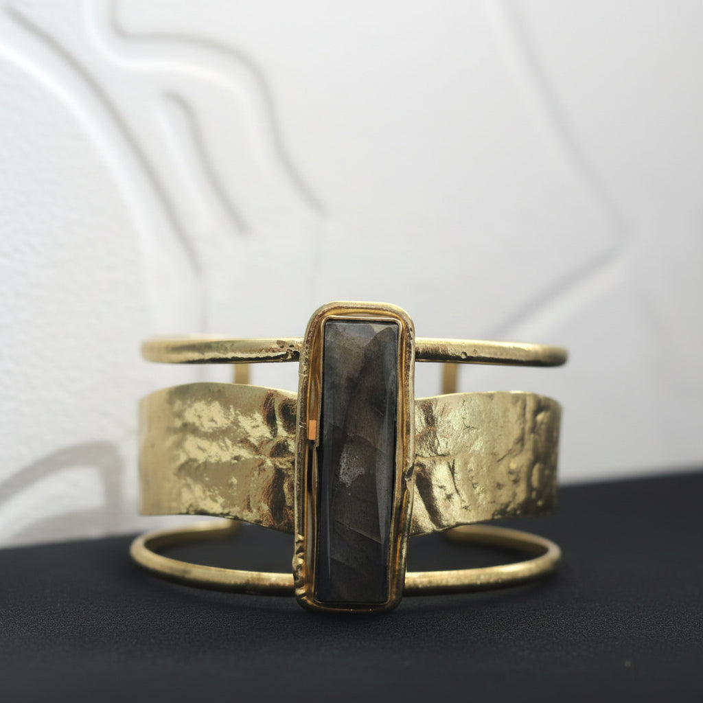 Gold bracelet with a central stone on a dark surface with a white blurred background ZoharasVogue