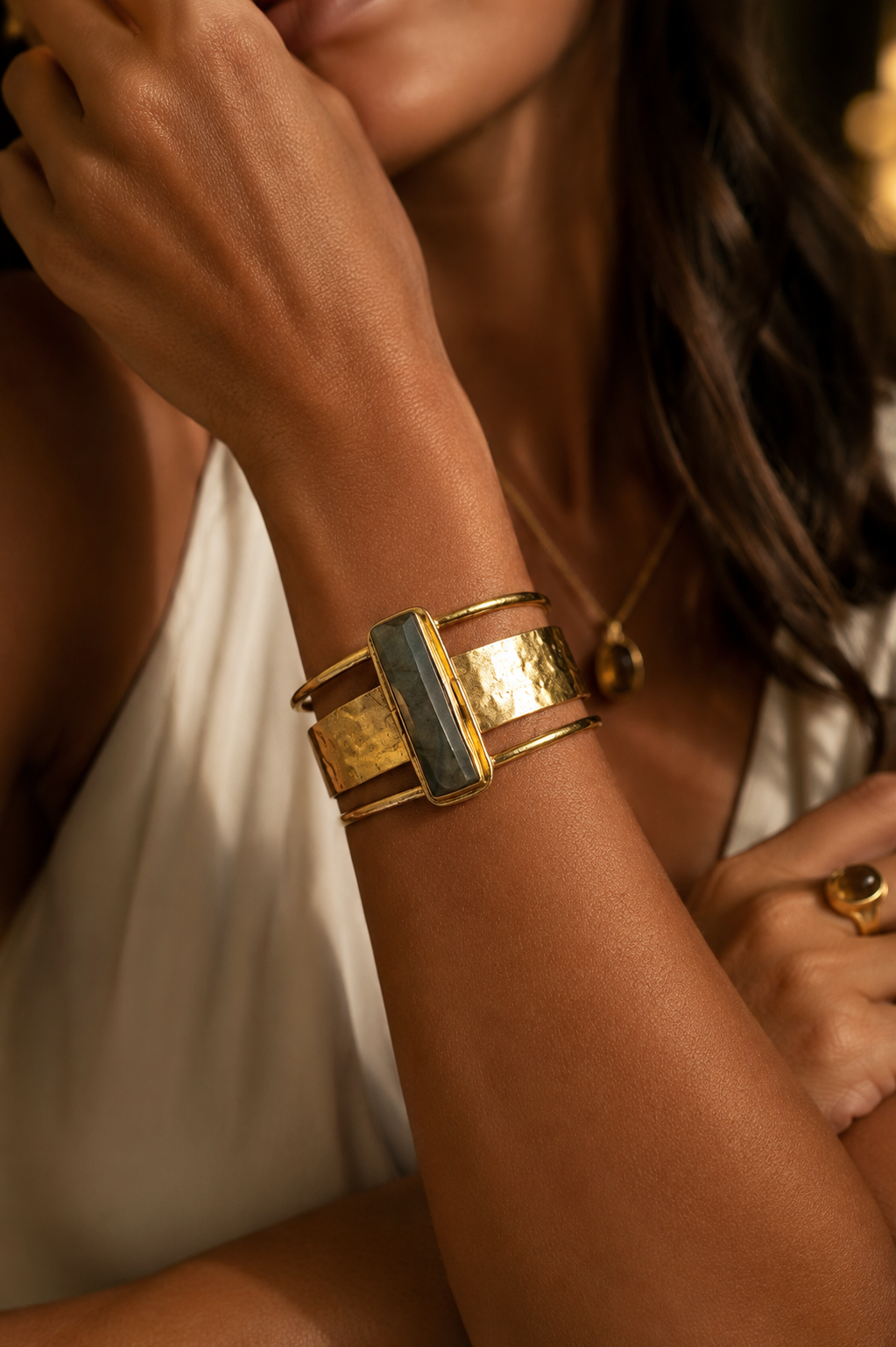 A model wearing a Labradorite_Gold bracelet with a central rectangular blue-green stone and thin red banded accents.