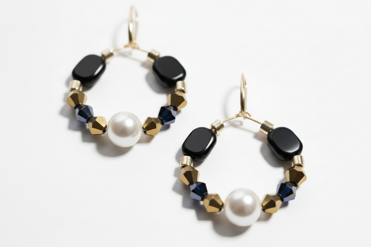 Gold hoop earrings featuring a central pearl, black geometric beads, navy crystal accents, and gold faceted spacer beads on a white background._ZoharasVogue