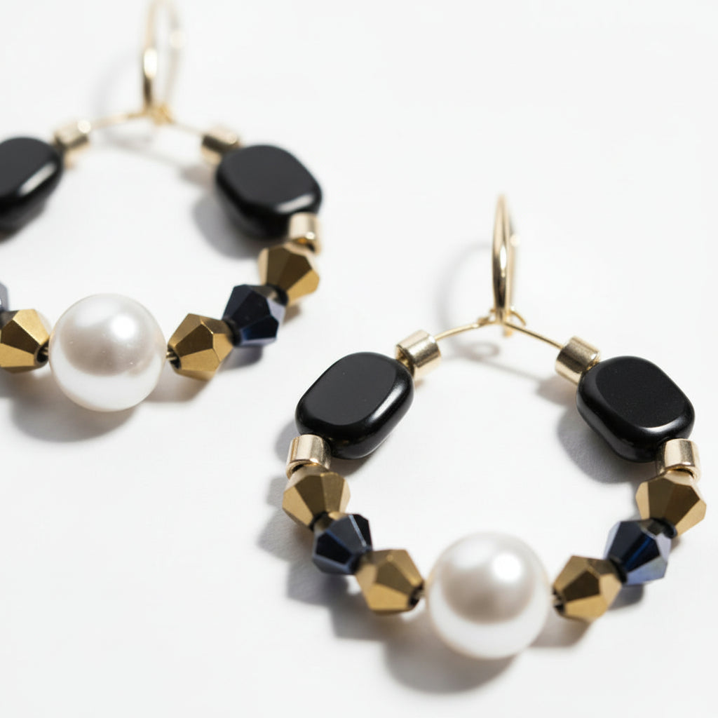 Gold hoop earrings featuring a central pearl, black geometric beads, navy crystal accents, and gold faceted spacer beads on a white background. ZoharasVogue