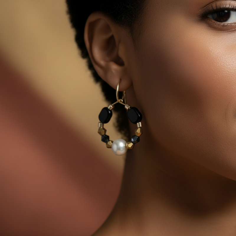 Gold hoop earrings featuring a central pearl, black geometric beads, navy crystal accents, and gold faceted spacer beads on a white background. ZoharasVogue