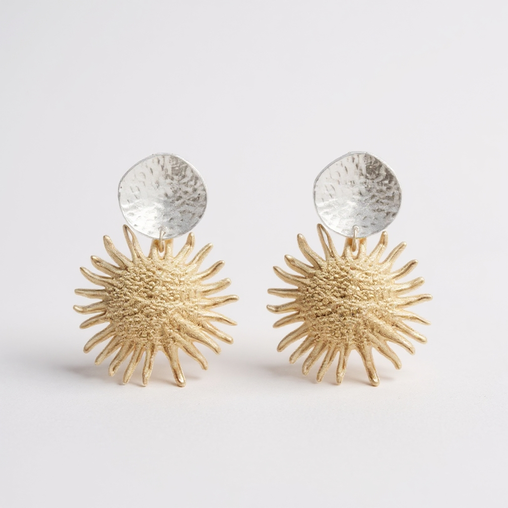 Pair of gold sunburst earrings with silver tops on a light gray background