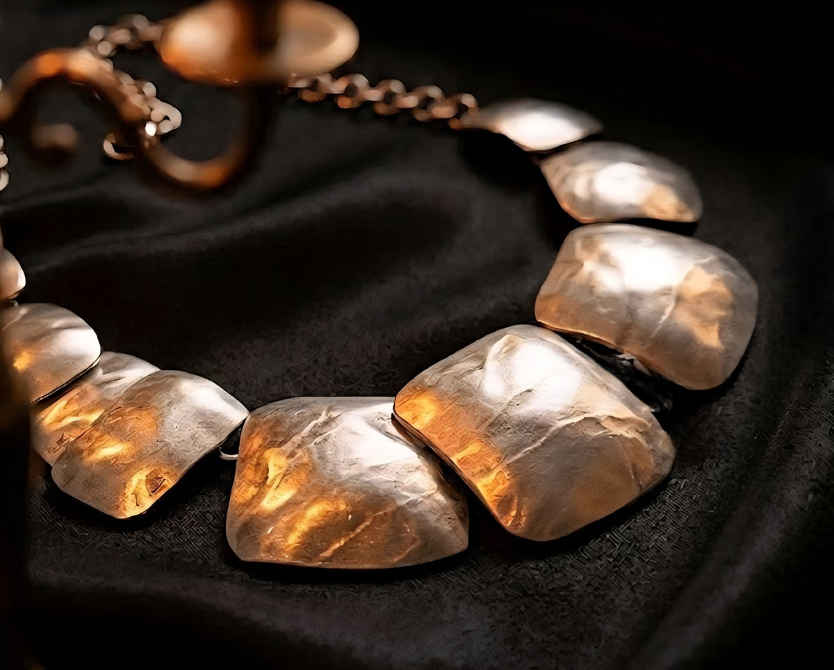 Close-up of a silver necklace with large, irregularly shaped links on a dark fabric background.