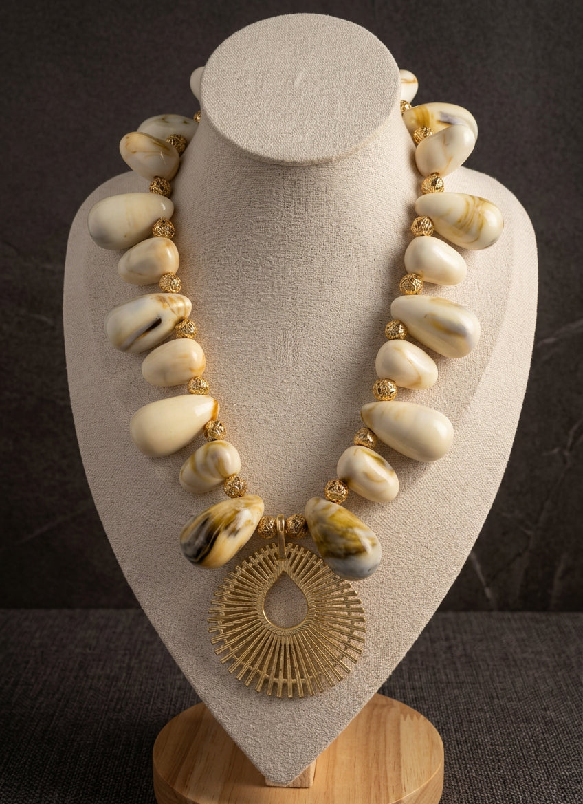 Solaya Sunburst Shell Necklace with ivory acrylic shell beads, gold-tone plated lava accents and an open teardrop sunburst pendant on a cream bust