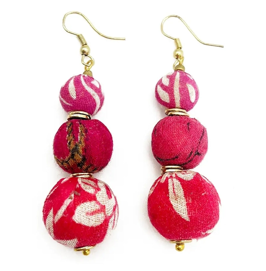 Close-up of handcrafted pink beaded earrings made from recycled sari fabric and wood, hanging against a neutral background