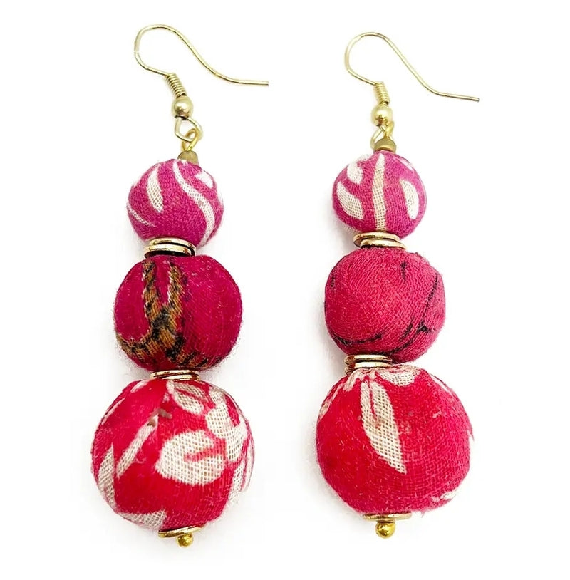 Close-up of handcrafted pink beaded earrings made from recycled sari fabric and wood, hanging against a neutral background