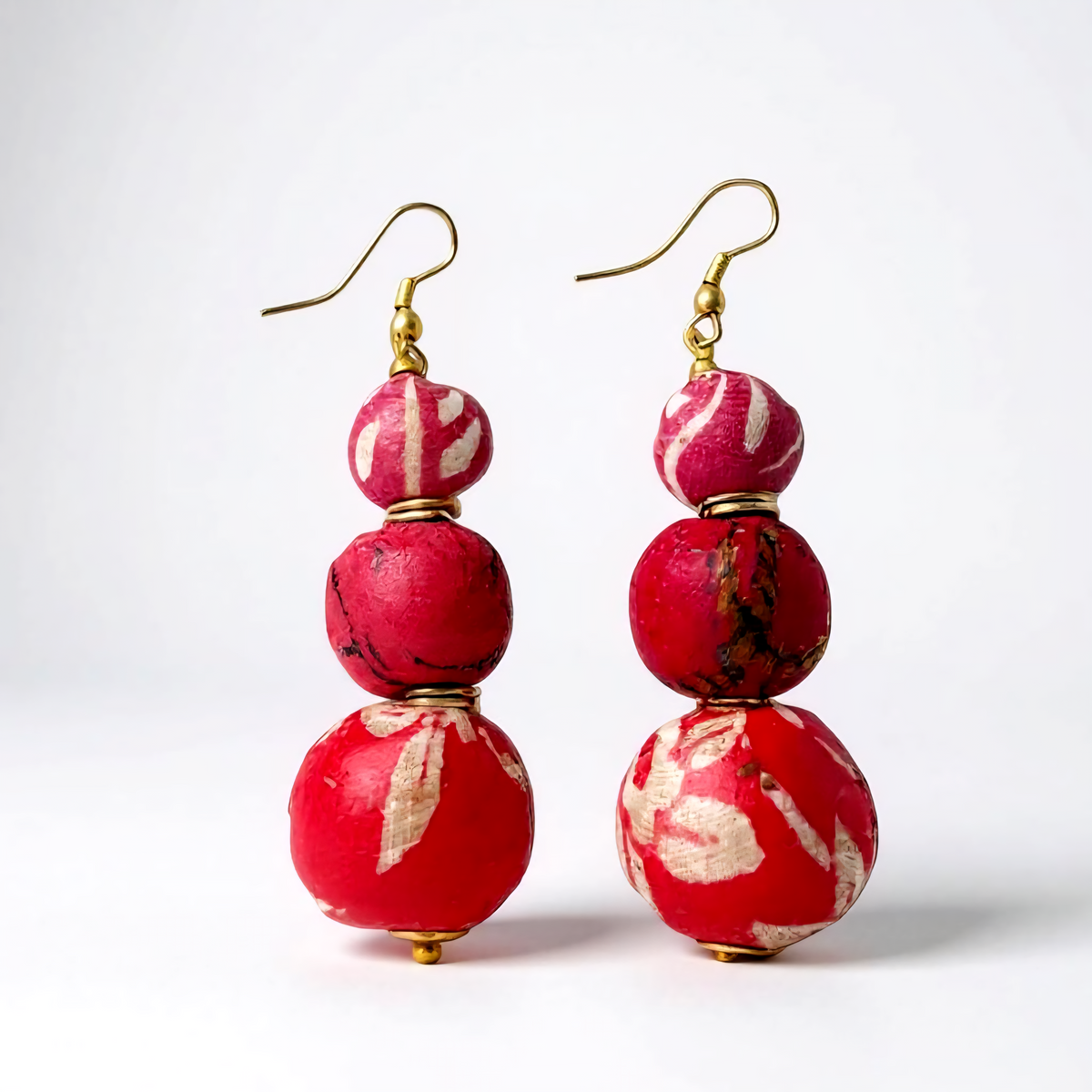 Close-up of handcrafted pink beaded earrings made from recycled sari fabric and wood, hanging against a neutral background.