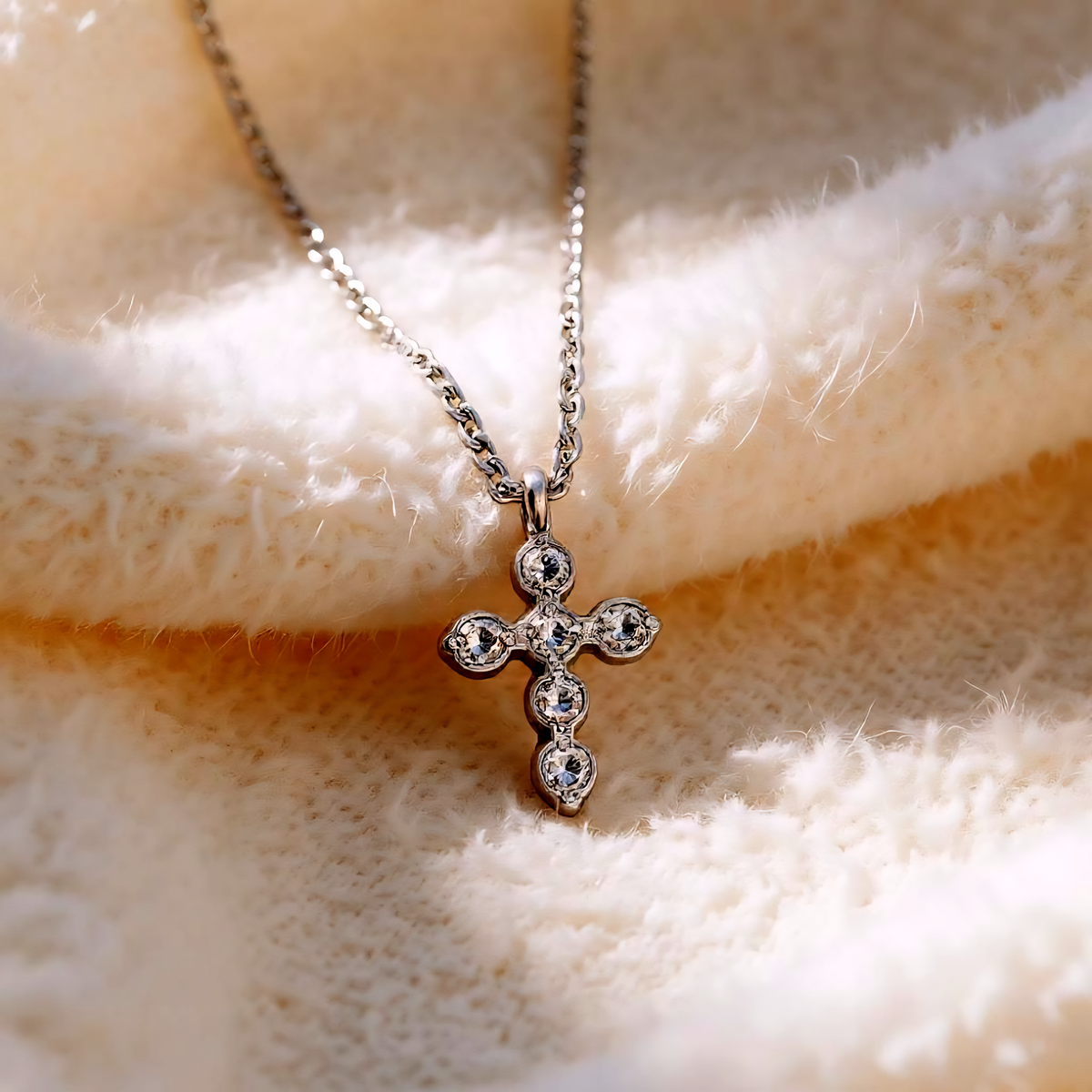 Silver cross pendant necklace on a textured beige surface