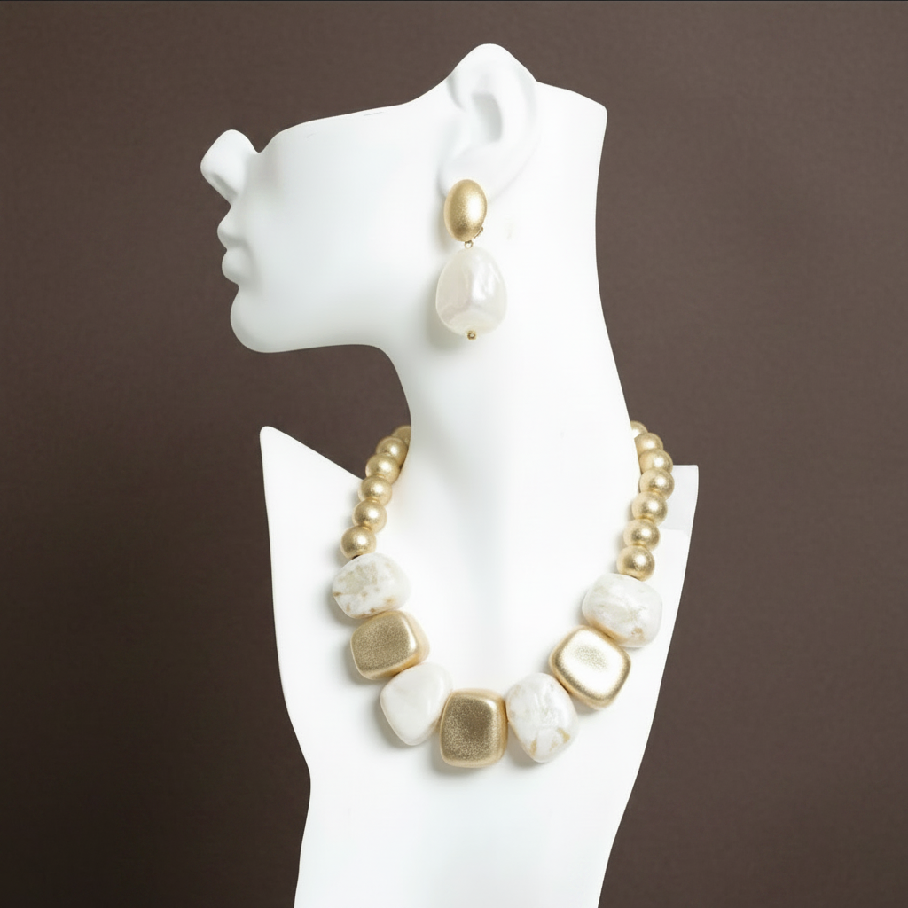 A chunky collar-style necklace featuring alternating matte gold nuggets and smooth, irregular marbled cream stones, resting on a white tufted surface. ZoharasVogue