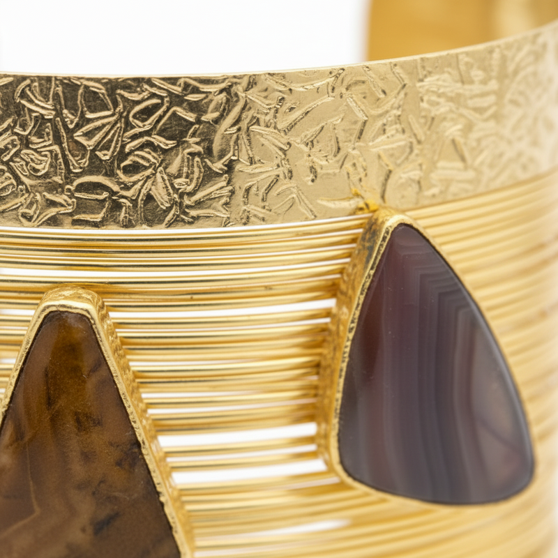 Gold bracelet with textured design and dark gemstones on a white background_The Obsidian Empress Cuff