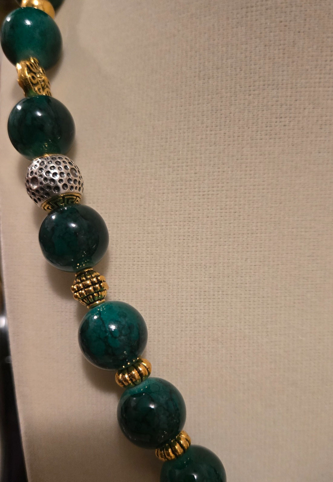 Close-up of dark green polished beads with gold and contrasting silver-tone accents