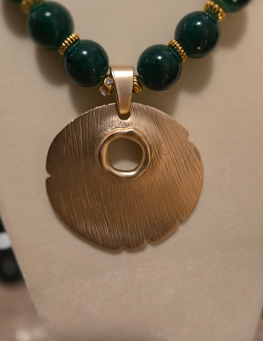 Close-up of organic gold-tone medallion pendant and dark green beads