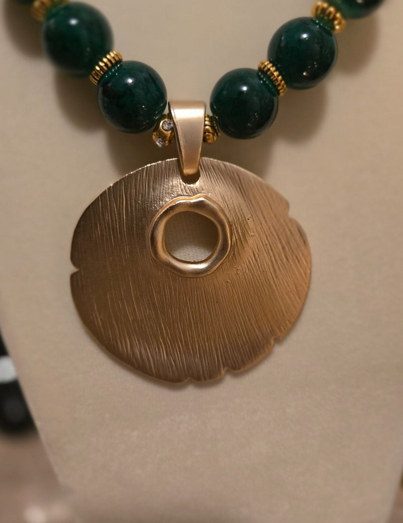 Close-up of organic gold-tone medallion pendant and dark green beads