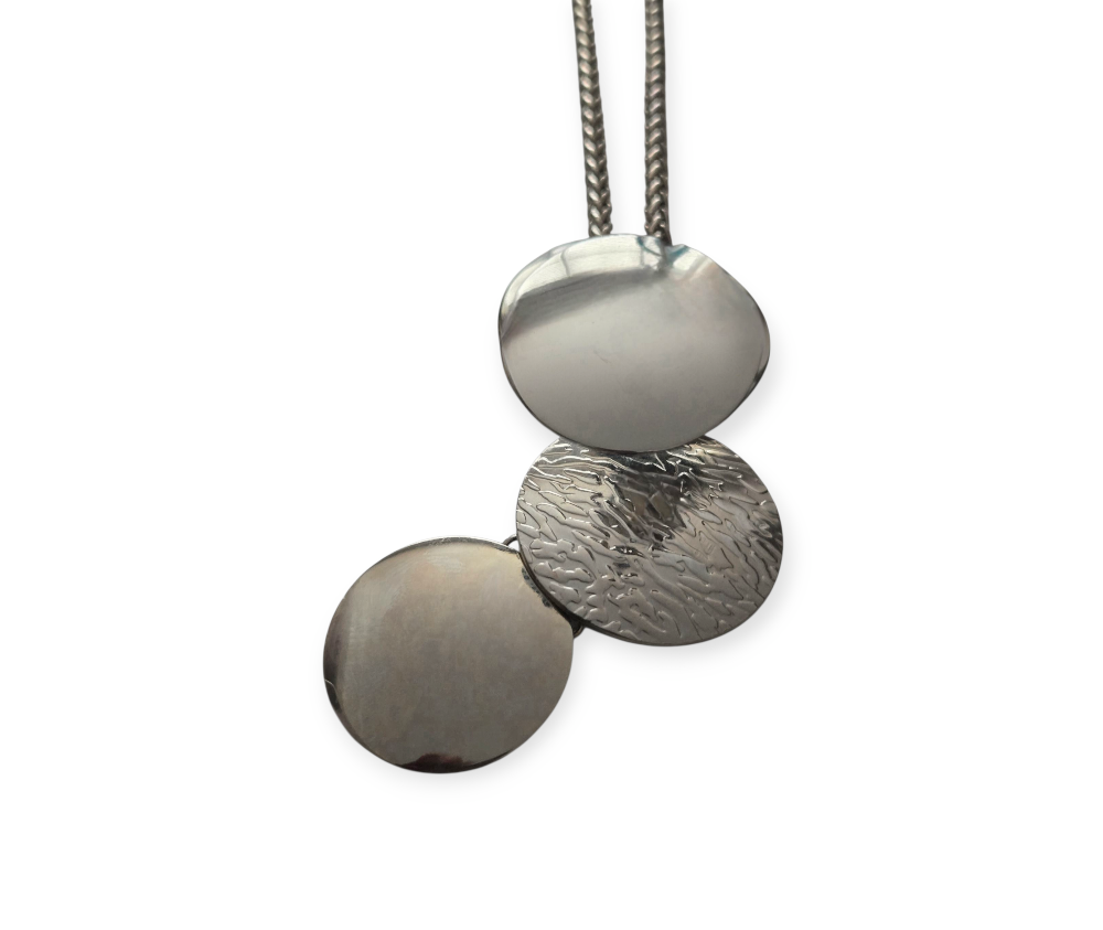 Long silver stainless steel necklace with three layered round pendants—polished, hammered, and matte—on a double chain, displayed on white background