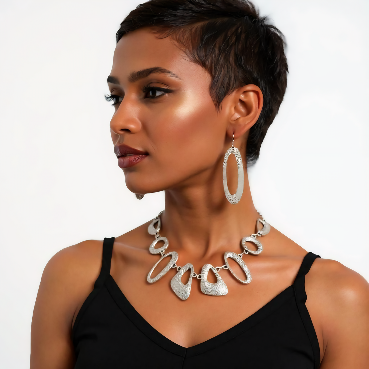 Woman wearing silver hoop earrings and a matching necklace on a plain background