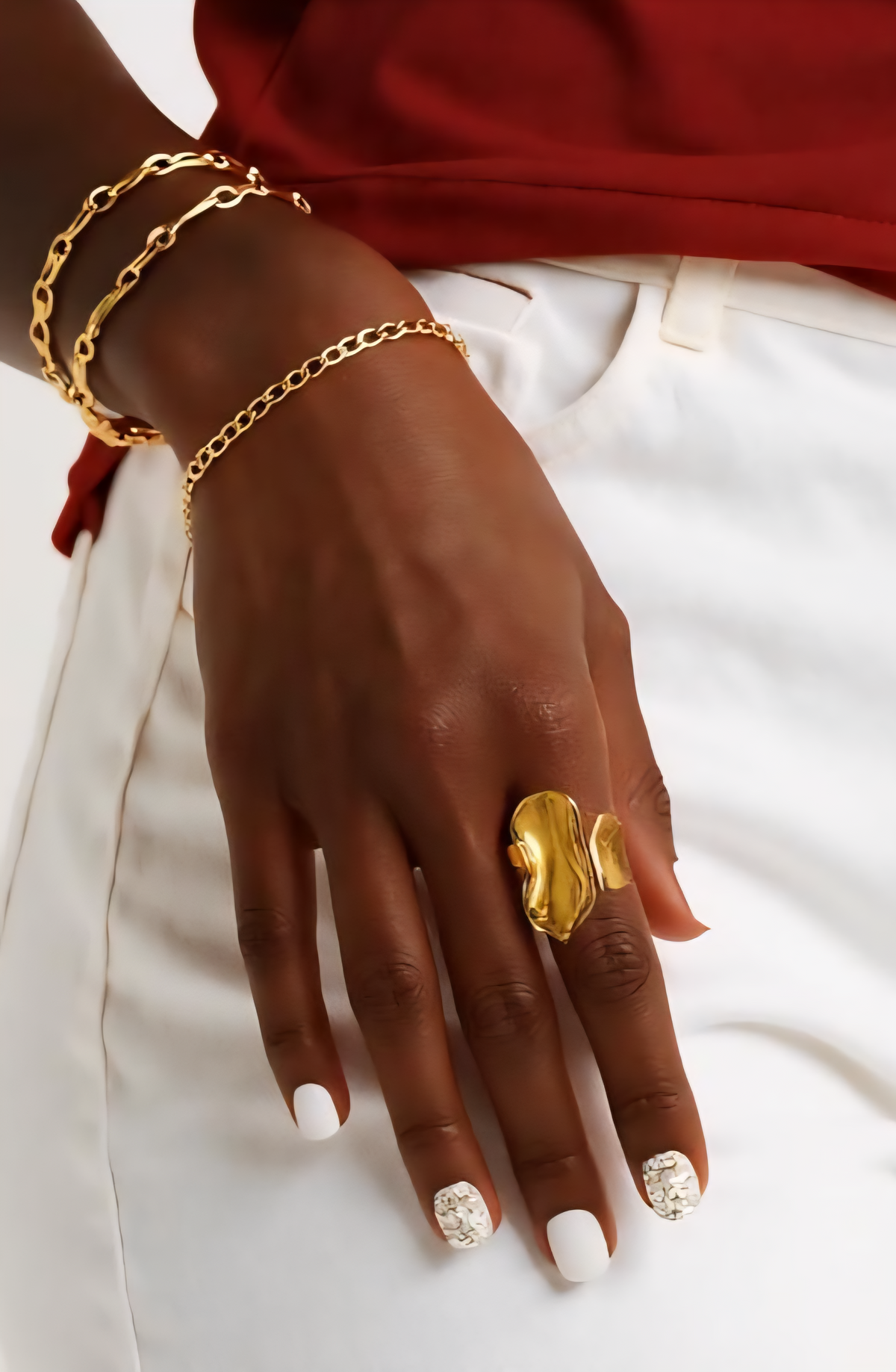 Close-up of a woman’s hand wearing the Aurora Flow 18K Gold Statement Ring with an abstract molten gold design, paired with a gold and pearl cuff bracelet. ZoharasVogue 