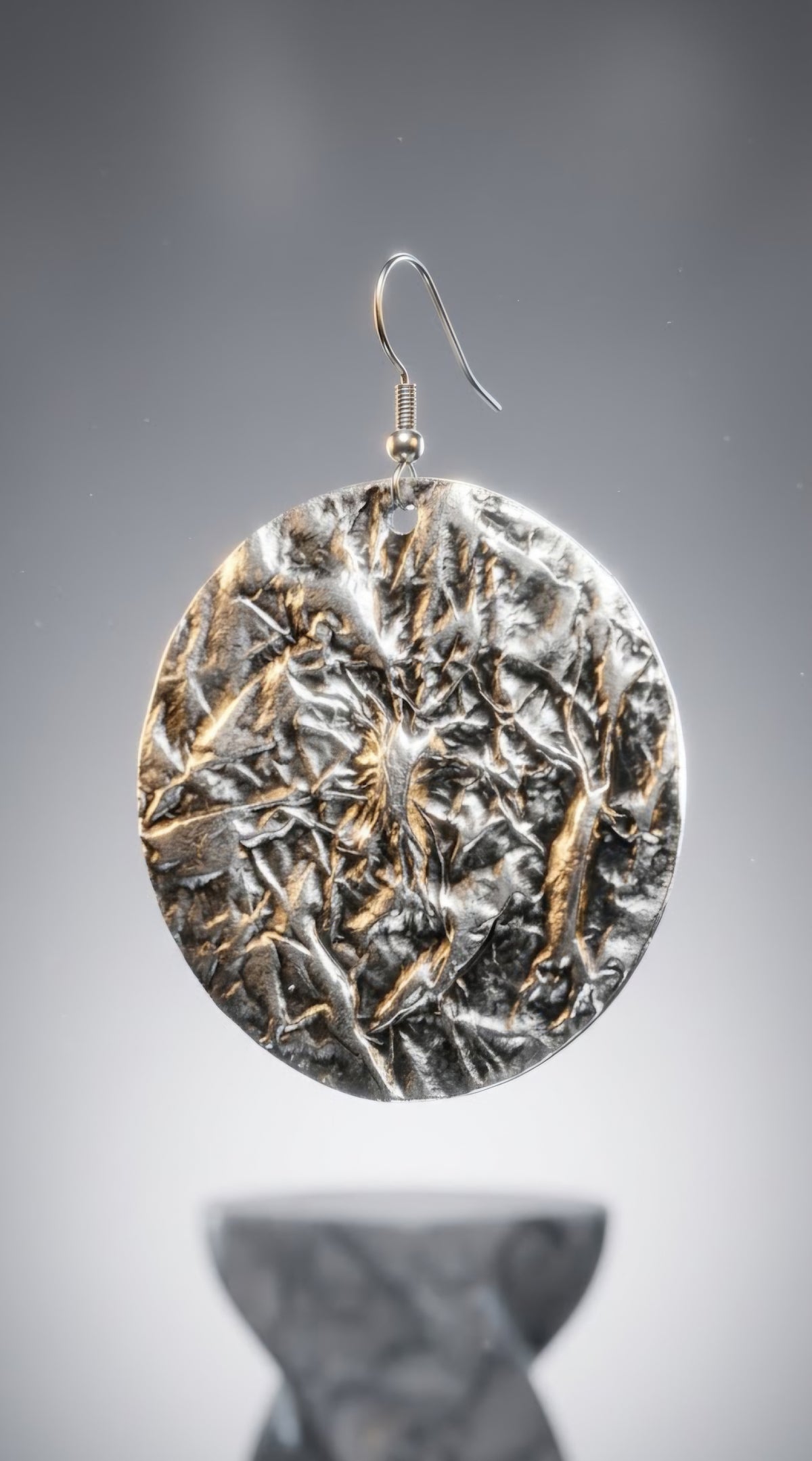 A premium 3D photorealistic render hero shot of a single Aura Textured Silver Disc Earring, suspended against a sophisticated soft gradient grey background. The close-up view emphasizes the deep, complex crumpled metal foil texture of the large silver circular disc, with dramatic studio lighting creating brilliant highlights and shadows across the multi-faceted surface.