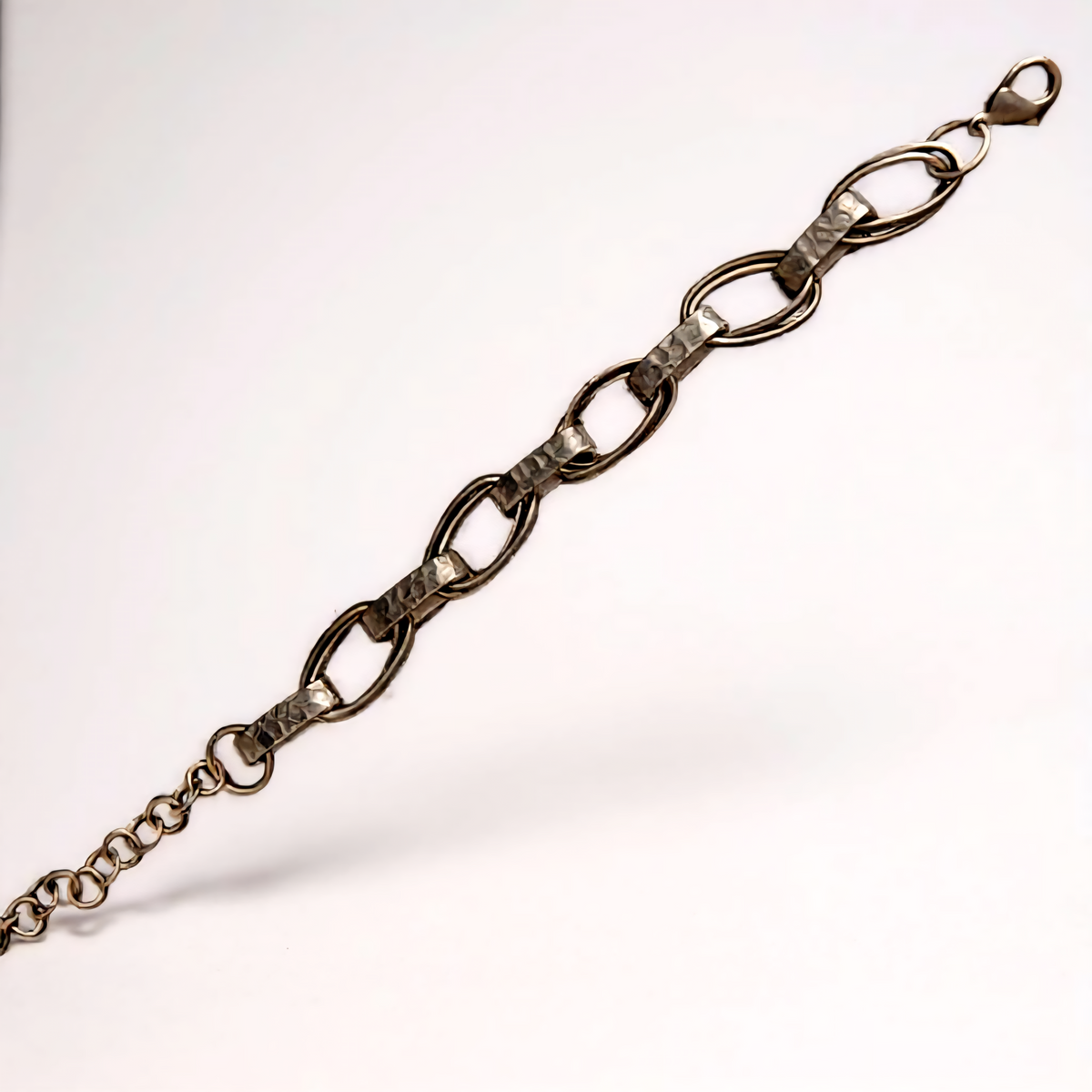 Obsidian Smoke Bracelet with hammered oval chain links in a smoky gunmetal-tone finish, accented by a single crystal detail at the clasp, styled for modern elegance. ZoharasVogue 